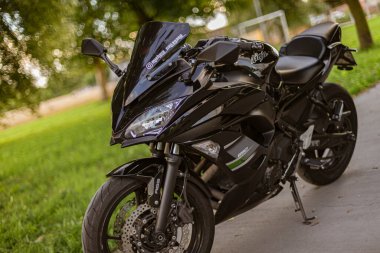 Milan, İtalya 4 Ekim 2024: Siyah bir kawasaki ninja 650 motosikleti arka planda yeşil çimenler ve ağaçlarla kaplı asfalt bir yüzeye park edilmiştir