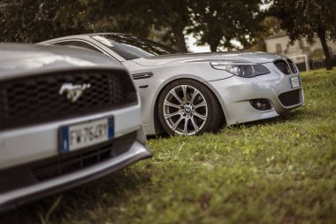 Milan, İtalya 4 Ekim 2024: Çimenli bir arazide yan yana park edilmiş gümüş bmw e60 ve gümüş bir Ford Mustang