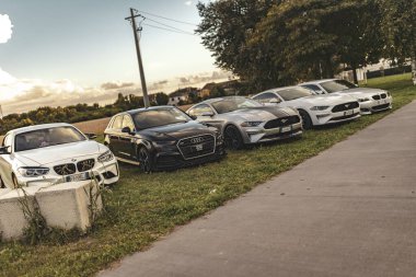 Milan, İtalya 4 Ekim 2024: Beş Alman lüks arabası ve bir Amerikan kaslı arabası bir otoparkın kenarındaki çimlerin üzerine park edildi