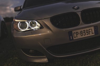 Milan, İtalya 4 Ekim 2024: Günbatımında farları parlayan modern araba ve arka planda başka bir araba