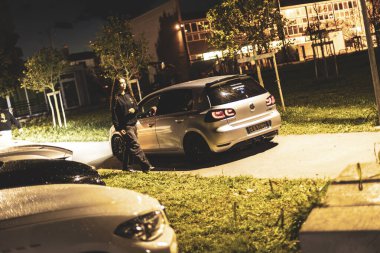 Milan, İtalya 4 Ekim 2024: Genç bir kadın geceleyin bir sokakta park edilmiş gümüş bir hatchback 'in yanından geçiyor