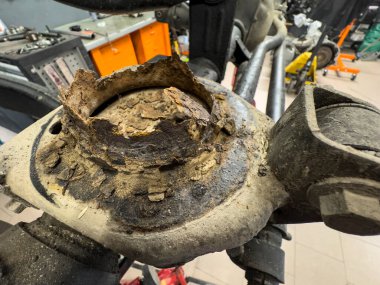 Ağır paslanmış bir araba süspansiyon kolunu kontrol eden bir tamirci araba tamirhanesinde tamire ihtiyaç duyuyor.