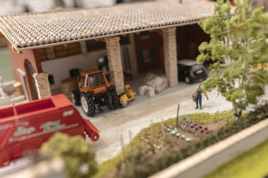 Milan, İtalya 8 Ekim 2024: Minyatür tarım malzemeleri sergilenen çiftlik modeli ve sebze bahçesiyle ilgilenen bir çiftçi