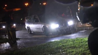 Milan, İtalya 4 Ekim 2024: Gri sedan BMW E36, yağmurlu ve kentsel yansımalarla çevrili, gece ıslak sokağı aydınlatan farlar parketti