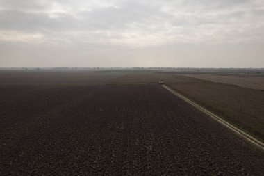 Bulutlu bir günde, yeni ekin ekimi için toprağı hazırlayan traktör tarlasının hava görüntüsü.