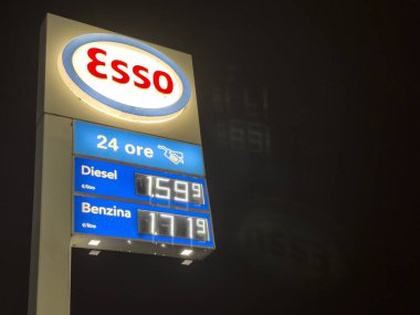 Villanova del Ghebbo, Italy 17 November 2024: Illuminated esso sign displaying gasoline and diesel prices at a gas station at night clipart