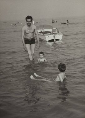 Roma, İtalya 1964 olabilir: 1960 'larda deniz kenarında yüzen oğulların 1960' larda yaz tatillerinin tadını çıkarırken babalarının denizdeki yüzüşünü izlediği klasik siyah beyaz fotoğraf