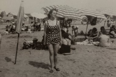 Roma, İtalya 1964: 1960 'larda kalabalık bir plajda benekli mayo giyen bir kadının klasik siyah beyaz fotoğrafı