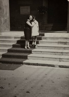Roma, İtalya 1964: Anne ve kızı, 20. yüzyılın ortalarından kalma iç açıcı siyah beyaz bir fotoğrafla zarif bir binanın girişinde kucaklaşıyorlar