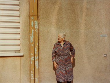 Roma, İtalya 1964 olabilir: 1970 'lerden kalma eski bir fotoğrafta yıpranmış bir duvar ve ofis kapısının yanında duran desenli bir elbise giyen yaşlı kadın
