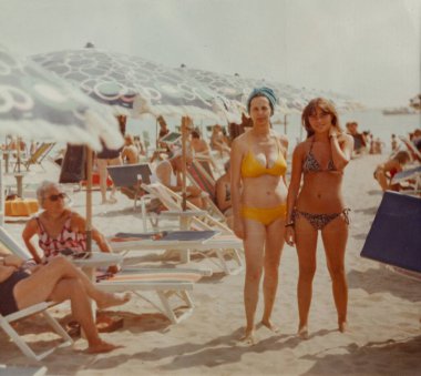Roma, İtalya 1964 olabilir: 1960 veya 1970 'lerden kalma klasik bir fotoğrafta, İtalya' da yaz aylarında kalabalık bir plajda bikini giyen iki kadın poz veriyor