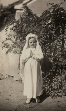 Roma, İtalya 1964: İlk komünyon kıyafetlerini giymiş genç bir kızın dua edişini gösteren siyah-beyaz bir klasik fotoğraf