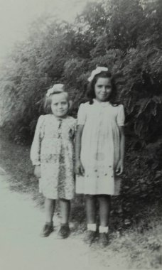 Roma, İtalya 1964 olabilir: Elbise ve kurdele takan iki kız, muhtemelen 1960 veya 1970 'lerde bir çitin önünde fotoğraf için poz veriyor