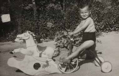Roma, İtalya 1964 olabilir: Arka bahçede sallanan bir atın yanında üç tekerlekli bisiklete binen bir çocuğun klasik siyah beyaz fotoğrafı, 20. yüzyılın ortalarından bir çocukluk sevincini yakalıyor.