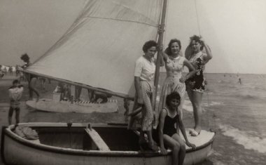 Roma, İtalya 1964 olabilir: 1960 'larda kalabalık bir plajda küçük bir yelkenlide poz veren dört genç kadın