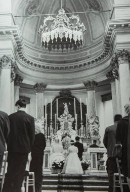 Roma, İtalya 1964 'te olabilir: Katolik kilisesinde bir düğün töreninin klasik siyah beyaz fotoğrafı, konuklar, çiçekçi kızlar ve büyük bir avize yer alıyor.