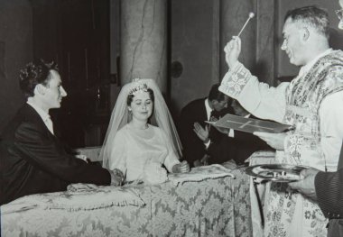 Roma, İtalya 1964 olabilir: Genç bir gelin ve damadın kilisede evlenirken çekilmiş klasik siyah beyaz fotoğrafı, rahip onları kutsadı.