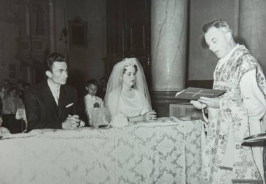 Roma, İtalya 1964 olabilir: Gelin ve damat düğün töreninde sunakta diz çökmüş, rahipler eski moda siyah beyaz eşlerden okuyor
