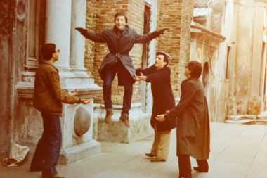 Roma, İtalya 1964: 70 'lerde İtalya' nın Venedik kentinde antik bir binanın yakınlarında genç bir adamı havaya uçururken eğlenen bir grup arkadaş