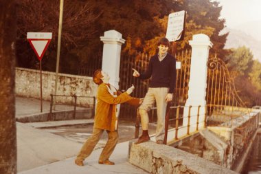 Roma, İtalya 1964 olabilir: İki genç adam otobüs durağında neşeli bir anın tadını çıkarıyorlar, 1970 'lerin kaygısız ruhunu yansıtan neşeli etkileşimleri.