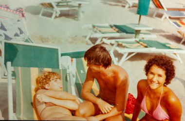 Roma, İtalya 1964 olabilir: 1970 'lerde güneşli bir yaz tatili sırasında plaj salonlarında gevşeyen ve sohbet eden üç genç arkadaş