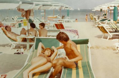 Roma, İtalya 1964: Yaz tatilinin tadını çıkaran genç bir çiftin plaj şemsiyelerinin altında çizgili plaj sandalyelerinde güneşlenirken çekilmiş fotoğrafı