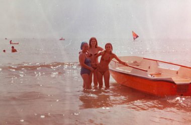 Roma, İtalya 1964 'te: Üç kadın yaz tatilinin tadını çıkarırken, arka planda diğer yüzücüler ve bir yelkenli ile küçük bir botun yanında denizde poz veriyorlar.