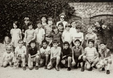 Roma, İtalya 1964 'te olabilir: 1970' lerde öğretmenleriyle birlikte tuğla ve sarmaşık duvarın önünde poz veren bir grup çocuğun klasik siyah beyaz fotoğrafı