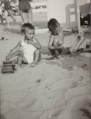 Roma, İtalya 1964 olabilir: 1960 'larda güneşli bir plajda oyuncak kamyonlarla oynayan iki genç çocuk çocukluk anılarını yakalıyorlar