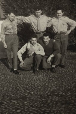 Roma, İtalya 1964 olabilir: Bir fotoğraf için birlikte poz veren beş üniformalı adam, bazıları ayakta ve diğerleri kaldırımlı bir avluda çömelmiş, muhtemelen 1960 veya 1970 'lerde çekilmiş