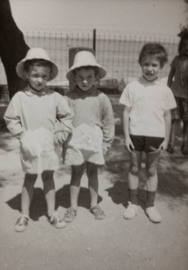 Roma, İtalya 1964 'te olabilir: Önlük ve şapka giyen iki çocuk, 1960' lardan veya 1970 'lerden kalma siyah ve beyaz renkli bir fotoğrafta şort ve tişört giyen başka bir çocuğun yanında duruyor.