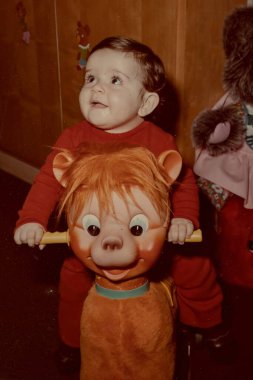 Roma, İtalya 1964: Erkek bebek 70 'lerin tarzında bir iç mekanda klasik sallanan at oyuncağıyla kırmızı oyunlar giyiyor