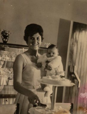 Roma, İtalya 1964: Doğum günü pastası keserken bebeğini tutan bir annenin klasik fotoğrafı