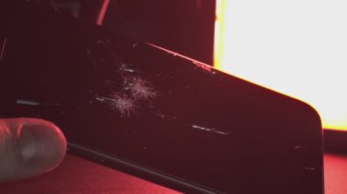 Adam elinde kırmızı ışığı yansıtan kırık ekranlı bir akıllı telefon tutuyor.