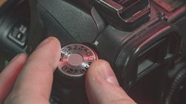 Profesyonel bir kamerada çekim modunu seçen bir fotoğrafçının yakın çekimi