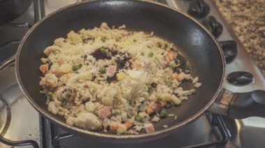 Şef tavada kızarmış pirinçle sebzeyi ahşap kaşık kullanarak karıştırıyor.