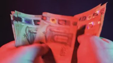 Kasiyer renkli ışıklar altında euro banknotlarını sayıyor