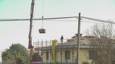 İşçiler çatıya tuğla kaldırmak için vinç kullanıyorlar.