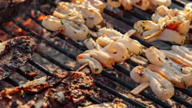 Taze mürekkep balığı şişleri, balıkların yanında sıcak kömürlerin üzerinde ızgara yapıyor.