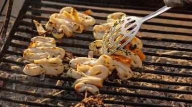 Şef mangalda kalamar şiş ızgara yapar, spatulayla onları çevirir.