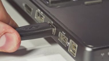 Teknisyen beyaz arka planda bir dizüstü bilgisayara USB kablosu takıyor.
