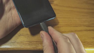 Adam masadaki bir cep telefonuna sürekli USB kablosu takıyor.