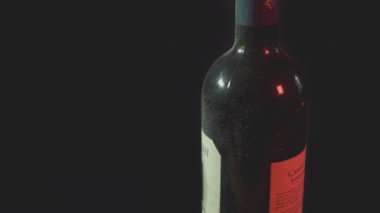 Yoğunlaşmayla parlayan şarap şişesinin yakın görüntüsü yavaşça siyah bir arkaplana doğru dönüyor.