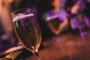 Badia Polesine, İtalya 14 Aralık 2024: Lale camlı beyaz köpük başlıklı altın biranın yenilenmesi, canlı bir pub ortamındaki ahşap bar tezgahında servis edildi