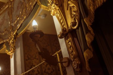 Badia Polesine, İtalya 14 Aralık 2024: Altın madalyalı bir opera kutusunu şık kumaş perdeleri ve altın püsküllü püsküllerle aydınlatan elektrik lambası