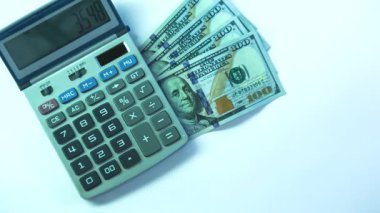 Milan, İtalya 1 Ocak 2025: Amerikan doları banknotları beyaz arka planda bir hesap makinesinin yanına düşüyor