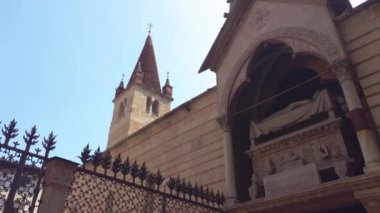 Verona, İtalya 1 Ocak 2025: İşlenmiş demir bir çitin yanından geçen kamera İtalya 'nın Verona kentindeki scaliger mezarlarını ve çan kulesini ortaya çıkardı.