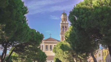 Rovigo, İtalya 1 Ocak 2025: Büyüleyici tarihi bir kilise, canlı ağaçlar ve huzur içinde gezinen insanlar ile pitoresk bir İtalyan caddesini ele geçirmek