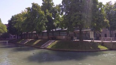 Treviso, İtalya 1 Ocak 2025: Duck Treviso, İtalya 'da ağaçlarla gölgelenmiş küçük bir binayı geçerek bir kanalda yüzüyor