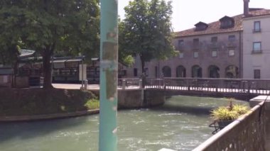 Treviso, İtalya 1 Ocak 2025: Kamera soldan sağa dönüyor Treviso, İtalya 'da bir kanal üzerinde bir köprü bulunan pitoresk bir şehir manzarası ortaya çıkarıyor